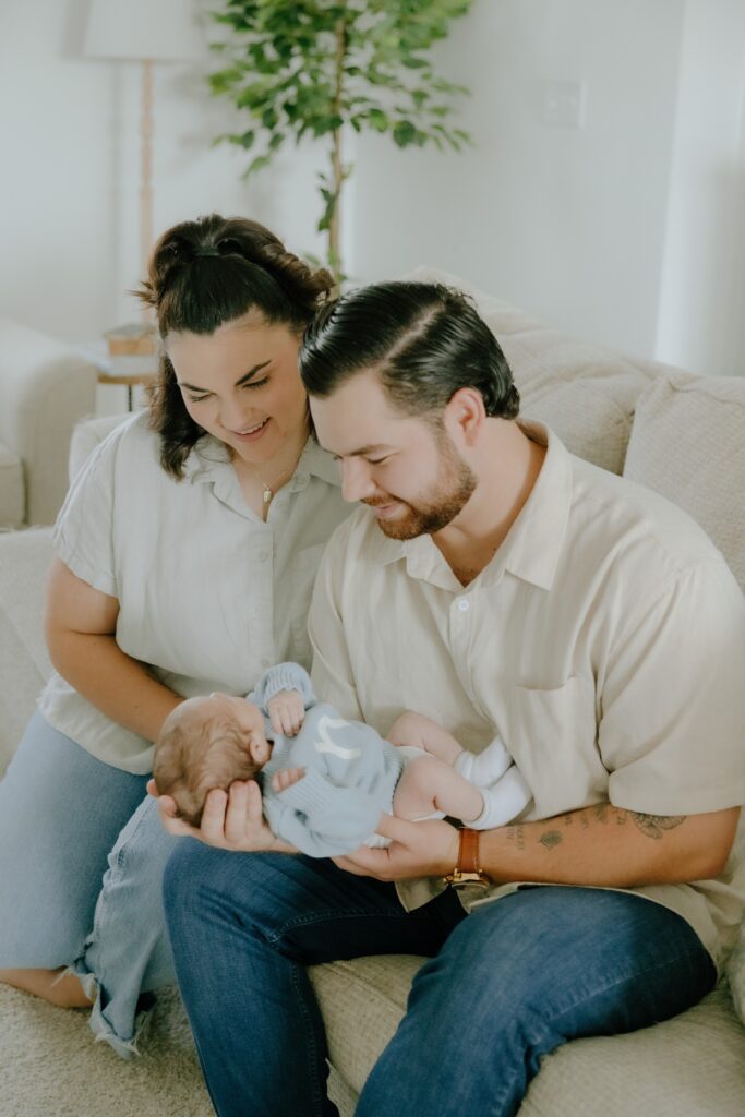 New parents smiling together while holding their newborn baby at home in Raleigh, North Carolina.