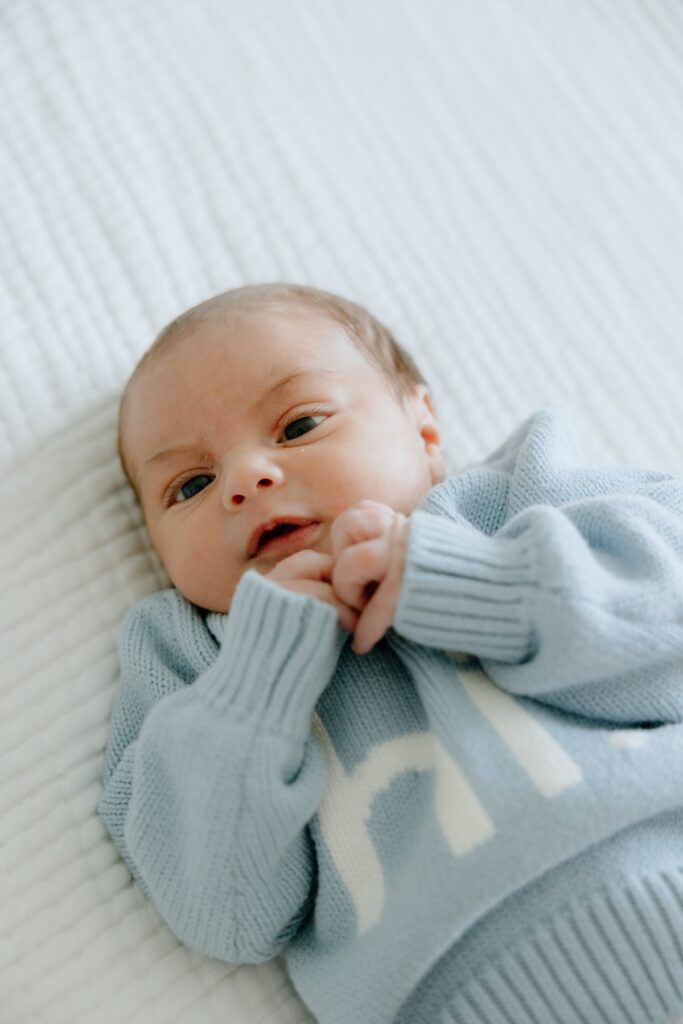 Close-up portrait of a newborn baby lying on a soft white blanket and wearing a blue knitted outfit.