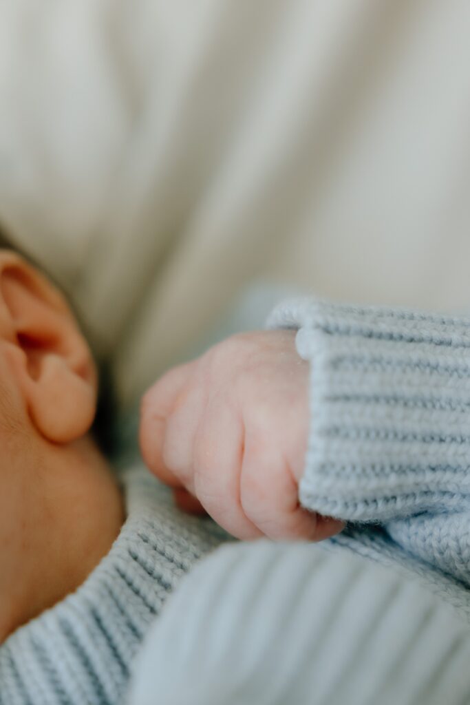 Close-up of a newborn baby's tiny hand and fingers in a soft blue knitted outfit